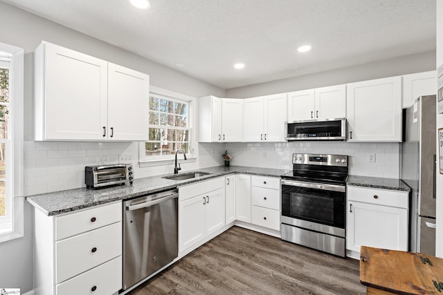 kitchen with a sink, dark stone countertops, appliances with stainless steel finishes, white cabinets, and dark wood-style flooring