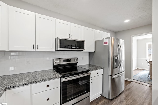 kitchen with tasteful backsplash, dark wood-style floors, white cabinetry, stainless steel appliances, and dark stone counters