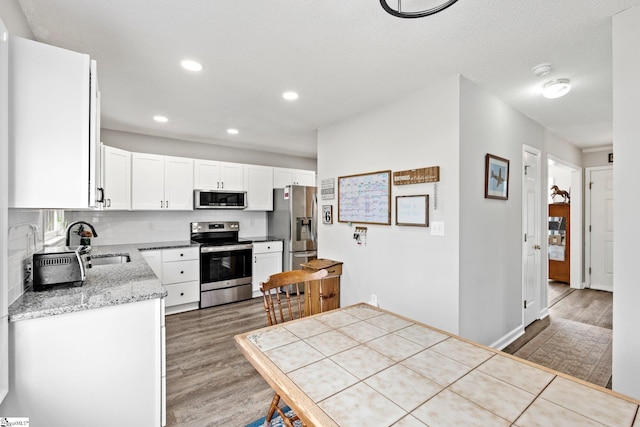 kitchen featuring backsplash, light wood-type flooring, white cabinets, stainless steel appliances, and a sink