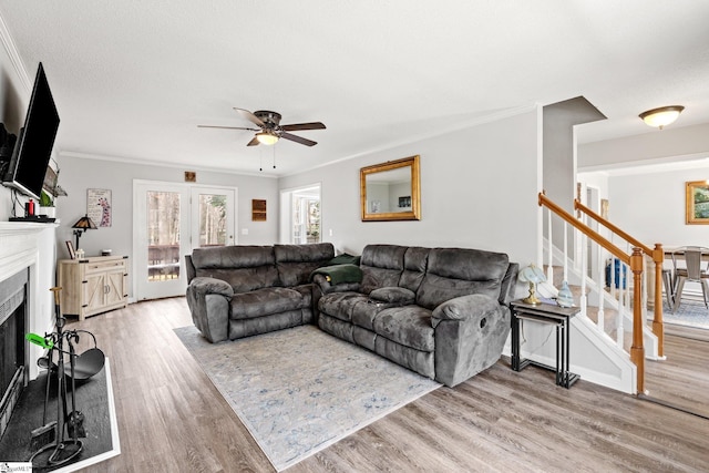 living room featuring stairway, a ceiling fan, wood finished floors, a fireplace, and crown molding