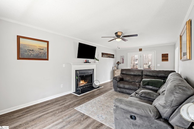 living room featuring ornamental molding, wood finished floors, baseboards, and a lit fireplace