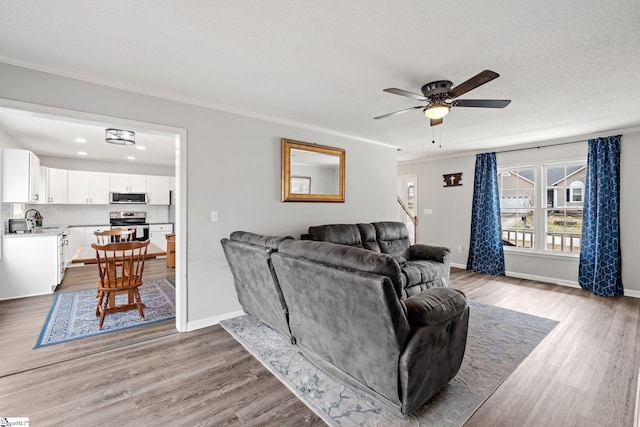 living area featuring a ceiling fan, baseboards, light wood-type flooring, and ornamental molding