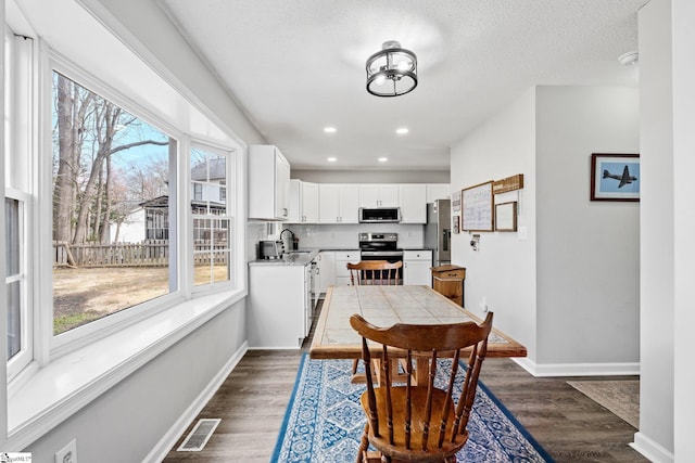 dining area with dark wood finished floors, baseboards, visible vents, and a textured ceiling