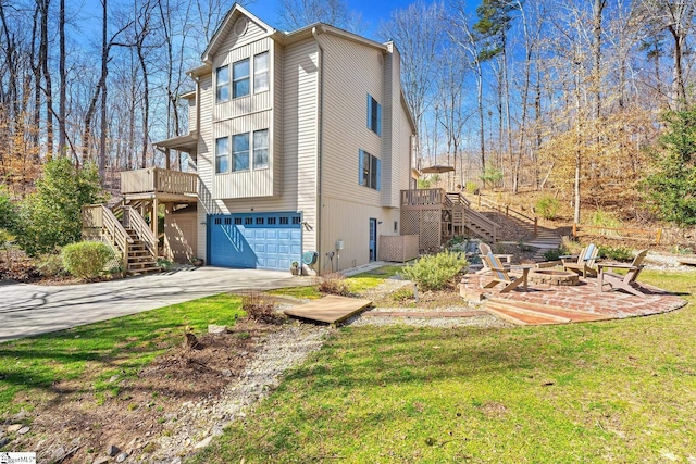 view of home's exterior with stairway, driveway, an outdoor fire pit, an attached garage, and a lawn