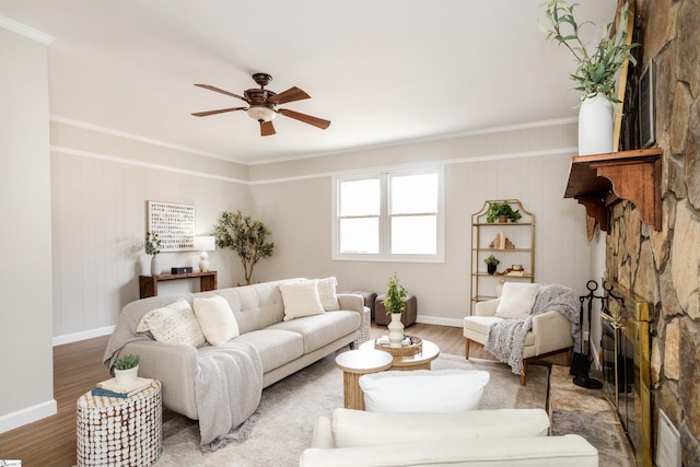 living room with a stone fireplace, ornamental molding, wood finished floors, and a ceiling fan