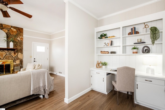 office space with ceiling fan, ornamental molding, built in desk, a fireplace, and wood finished floors