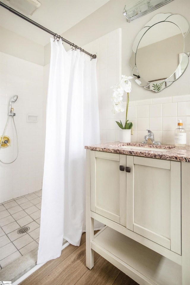 bathroom with visible vents, wood finished floors, vanity, and a tile shower