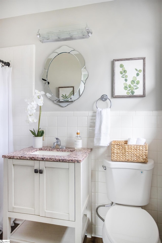 bathroom with a wainscoted wall, toilet, tile walls, and vanity