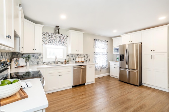 kitchen with a sink, decorative backsplash, stainless steel appliances, white cabinets, and light wood-style floors