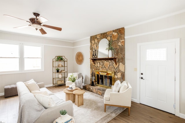 living room with wood finished floors, baseboards, a ceiling fan, a stone fireplace, and crown molding