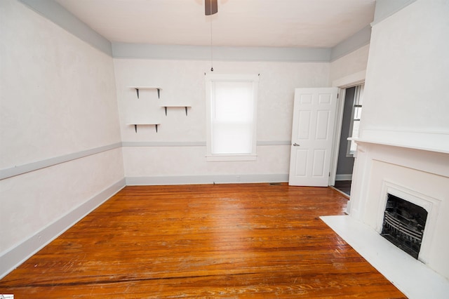 interior space with a fireplace, wood finished floors, baseboards, and a ceiling fan