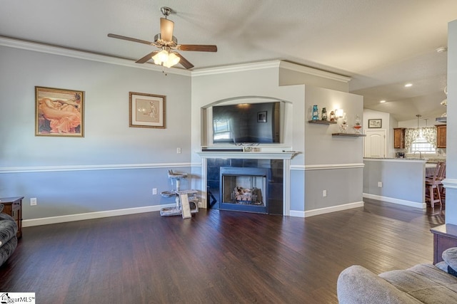 living area featuring crown molding, ceiling fan, baseboards, a tiled fireplace, and wood finished floors