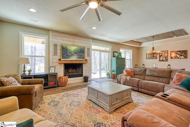 living room with visible vents, a large fireplace, light wood-style flooring, ceiling fan with notable chandelier, and a textured ceiling