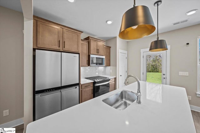 kitchen featuring visible vents, a sink, tasteful backsplash, stainless steel appliances, and hanging light fixtures