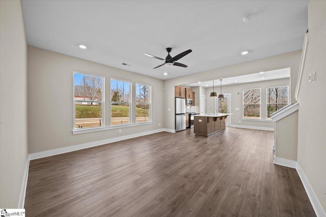 unfurnished living room with visible vents, baseboards, ceiling fan, and dark wood-style flooring