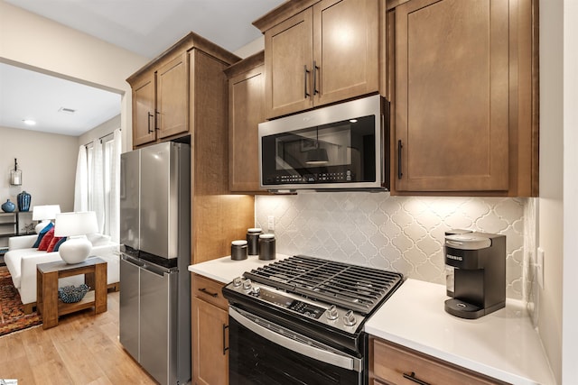 kitchen featuring decorative backsplash, light countertops, light wood finished floors, and stainless steel appliances