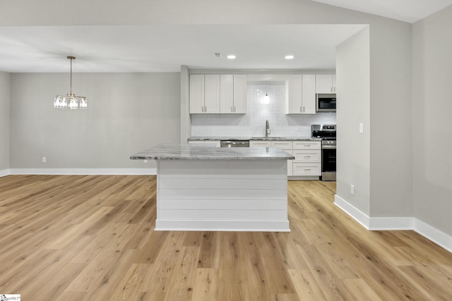 kitchen with light wood-type flooring, a sink, appliances with stainless steel finishes, decorative backsplash, and baseboards