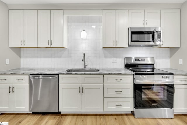 kitchen featuring light wood-style flooring, appliances with stainless steel finishes, light stone countertops, and a sink