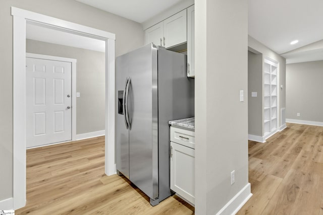 kitchen with light wood finished floors, visible vents, baseboards, stainless steel fridge with ice dispenser, and white cabinetry