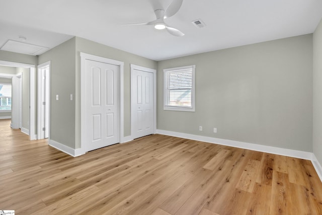 unfurnished bedroom featuring visible vents, two closets, light wood-style flooring, baseboards, and attic access