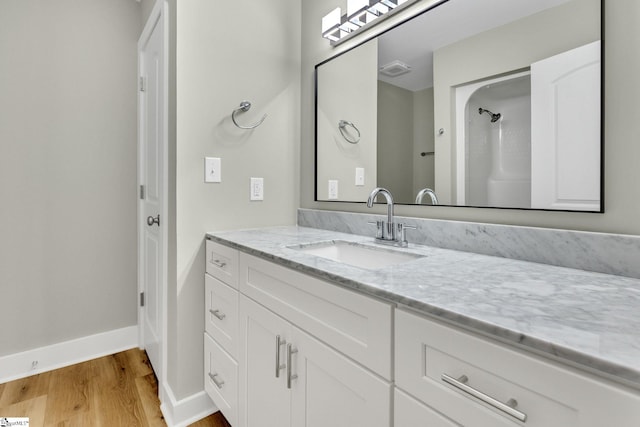 full bath featuring vanity, a shower, baseboards, and wood finished floors