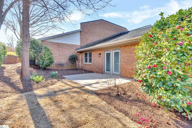 rear view of house featuring a patio, brick siding, and a shingled roof