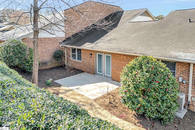 rear view of house featuring brick siding, a shingled roof, and a patio