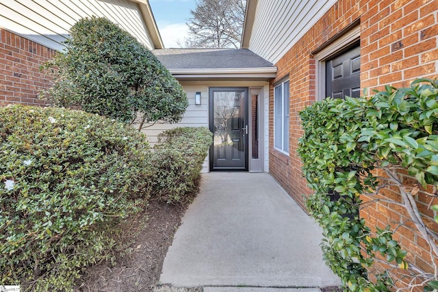 view of exterior entry with brick siding and roof with shingles