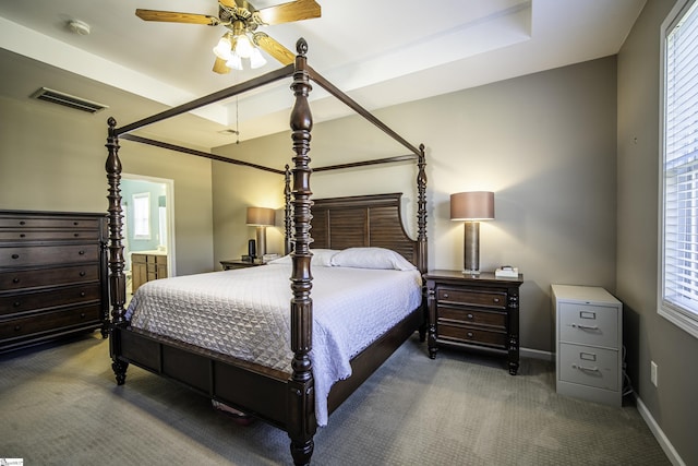 carpeted bedroom featuring a raised ceiling, baseboards, visible vents, and ensuite bathroom