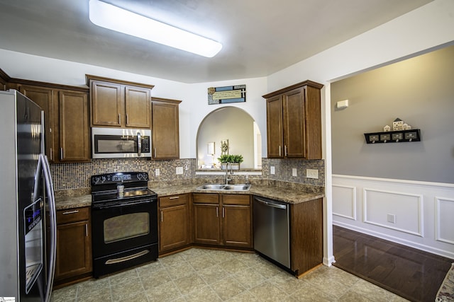 kitchen with a wainscoted wall, a sink, tasteful backsplash, arched walkways, and appliances with stainless steel finishes