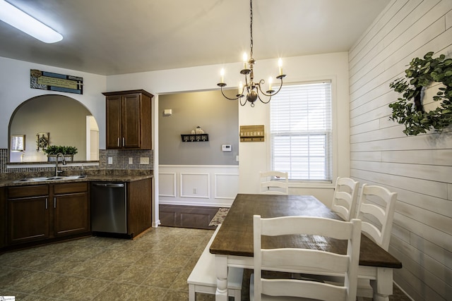 kitchen featuring arched walkways, a sink, dark brown cabinets, dishwasher, and a chandelier