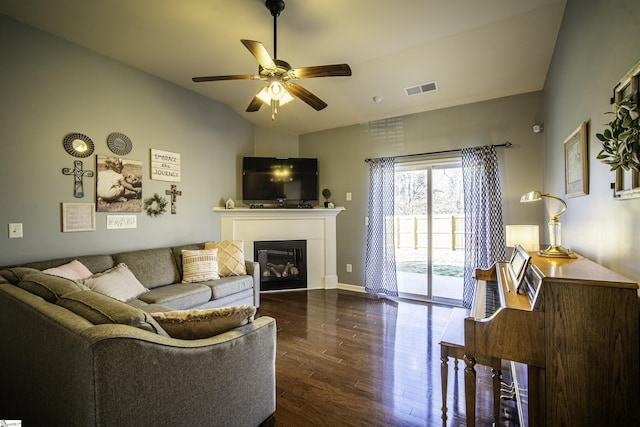 living room with visible vents, ceiling fan, vaulted ceiling, a glass covered fireplace, and dark wood-style flooring