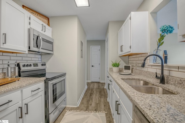 kitchen featuring light stone countertops, appliances with stainless steel finishes, white cabinetry, and a sink