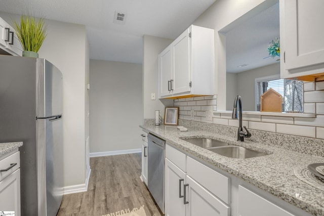 kitchen featuring light wood-type flooring, a sink, tasteful backsplash, white cabinetry, and appliances with stainless steel finishes