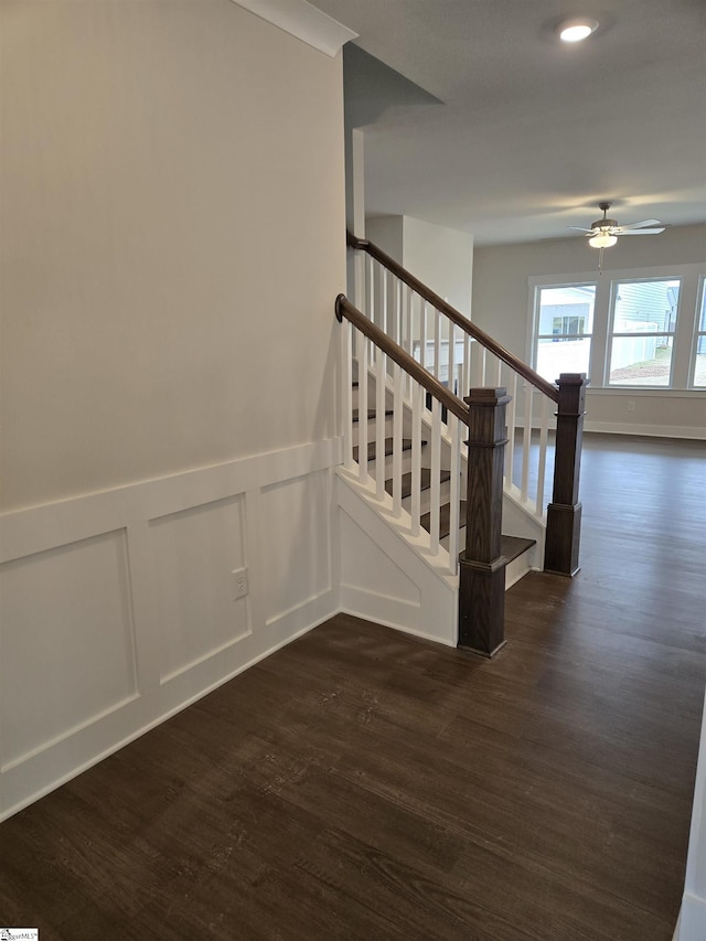 stairs featuring a decorative wall, wainscoting, a ceiling fan, and wood finished floors