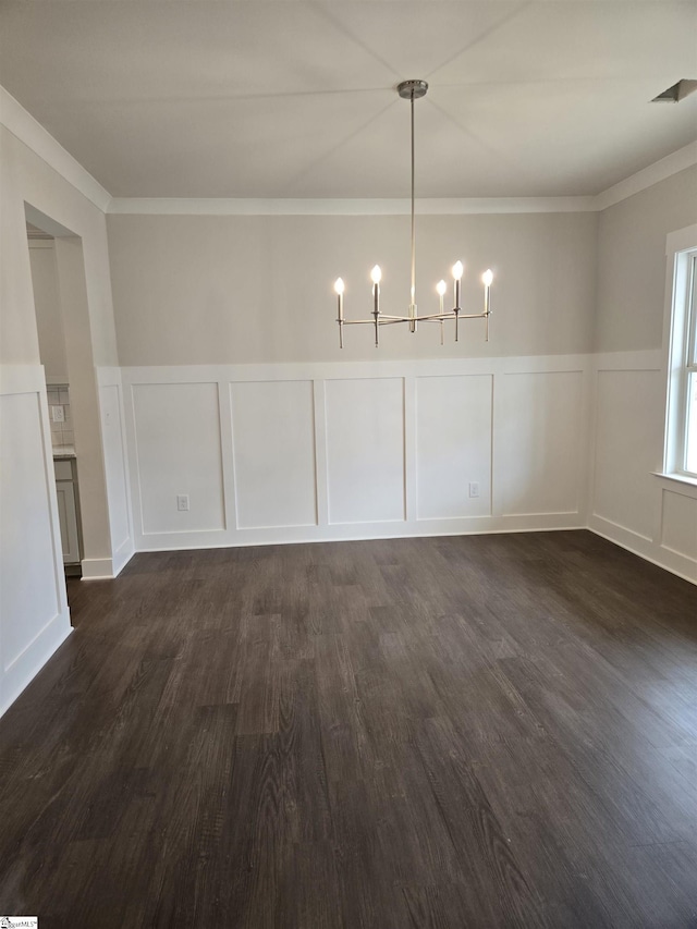 unfurnished dining area with dark wood finished floors, a decorative wall, an inviting chandelier, and ornamental molding