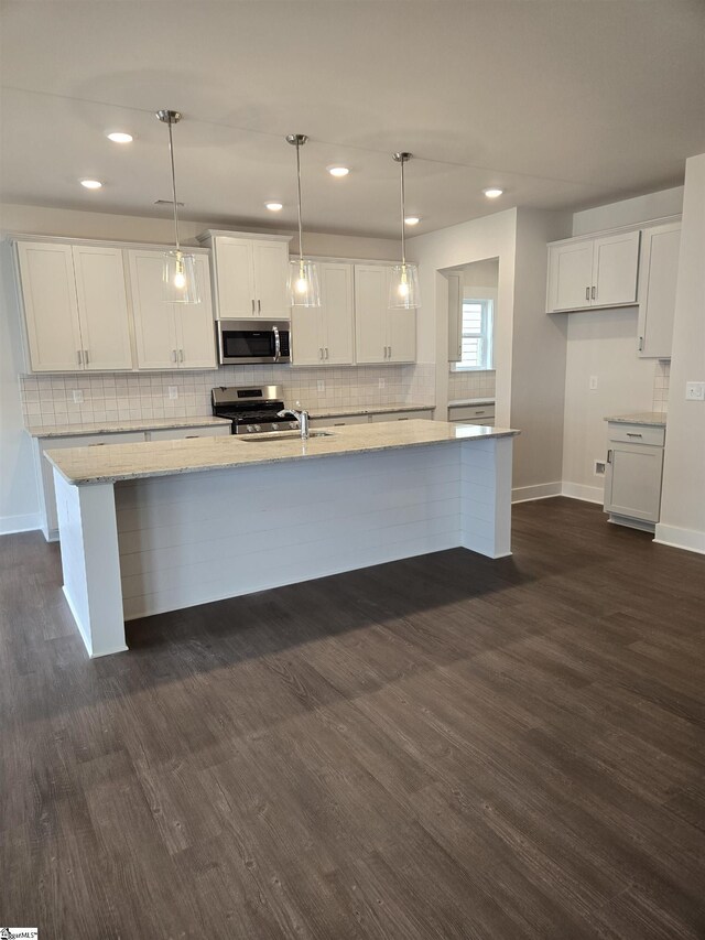 kitchen with dark wood finished floors, a large island, white cabinets, appliances with stainless steel finishes, and backsplash