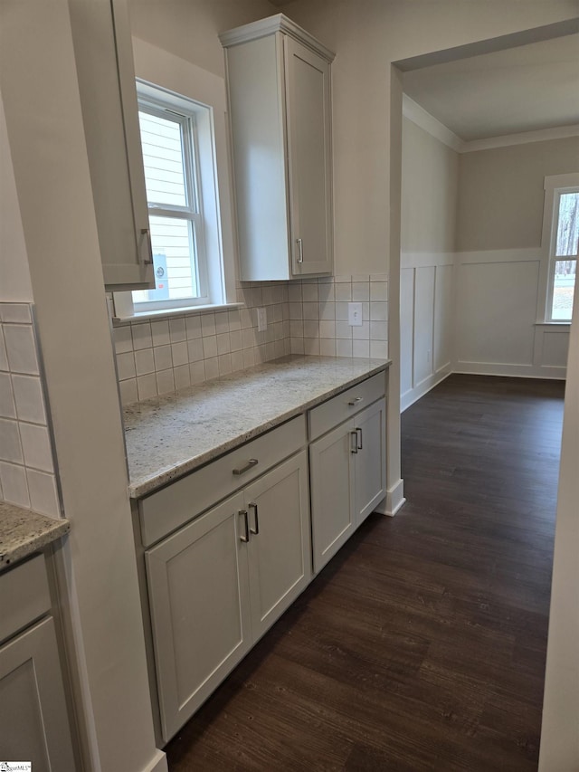 kitchen with wainscoting, light stone countertops, ornamental molding, and dark wood-style flooring