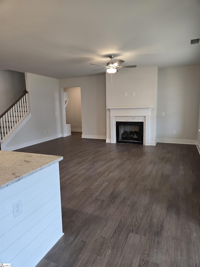 unfurnished living room with dark wood-style floors, baseboards, a fireplace, ceiling fan, and stairs