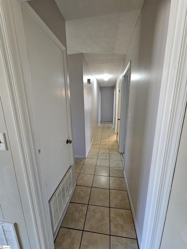 hallway featuring light tile patterned floors, visible vents, a textured ceiling, and baseboards