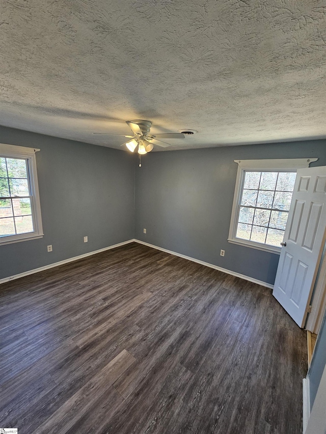 empty room featuring a textured ceiling, baseboards, and dark wood-style flooring