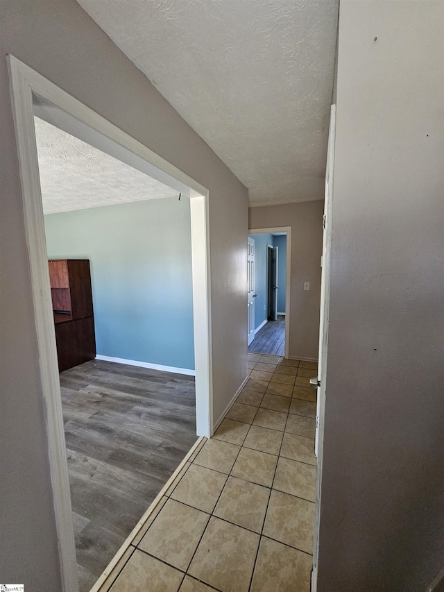 hall featuring light tile patterned floors, baseboards, and a textured ceiling