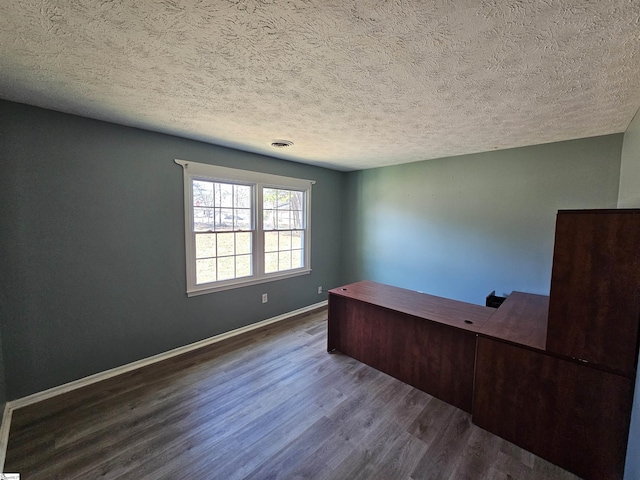 unfurnished office with a textured ceiling, dark wood-style floors, visible vents, and baseboards