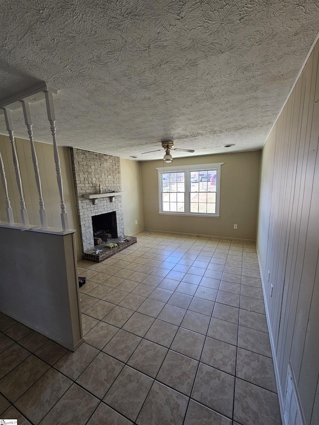 unfurnished living room featuring tile patterned flooring, visible vents, a brick fireplace, ceiling fan, and a textured ceiling