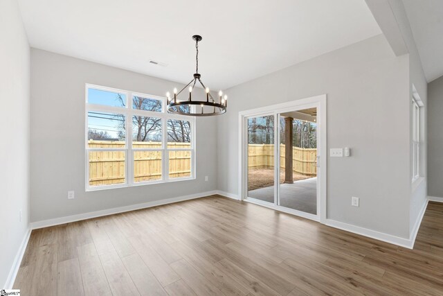 unfurnished dining area with wood finished floors, baseboards, a wealth of natural light, and a chandelier