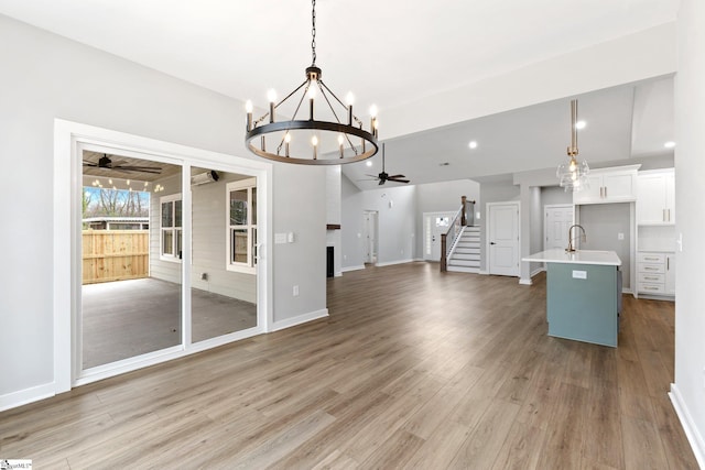 interior space with light wood finished floors, stairs, lofted ceiling, ceiling fan with notable chandelier, and a sink