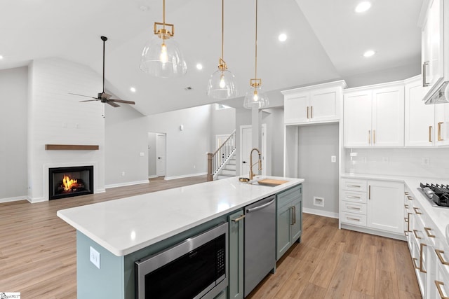 kitchen with an island with sink, a sink, light countertops, white cabinets, and appliances with stainless steel finishes