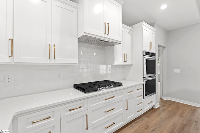 kitchen featuring light wood finished floors, under cabinet range hood, decorative backsplash, appliances with stainless steel finishes, and white cabinetry