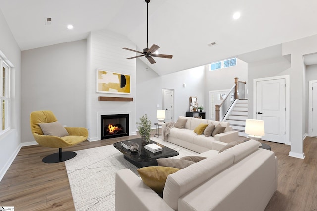 living room featuring stairway, wood finished floors, baseboards, high vaulted ceiling, and a large fireplace