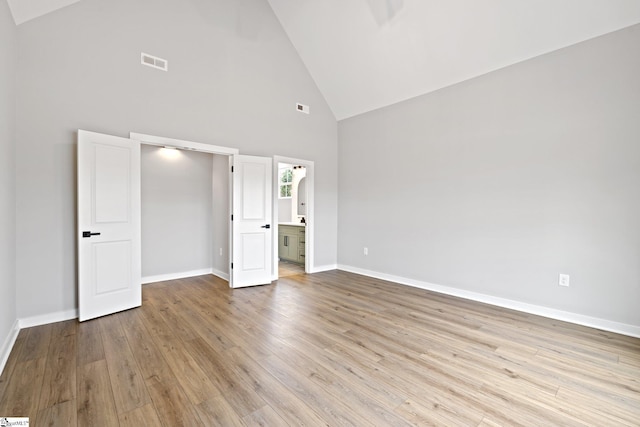 unfurnished bedroom featuring wood finished floors, visible vents, baseboards, high vaulted ceiling, and ensuite bath